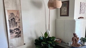 Een woonkamer met een groot schilderij, een vloerlamp, een Boeddhabeeld en een potplant.