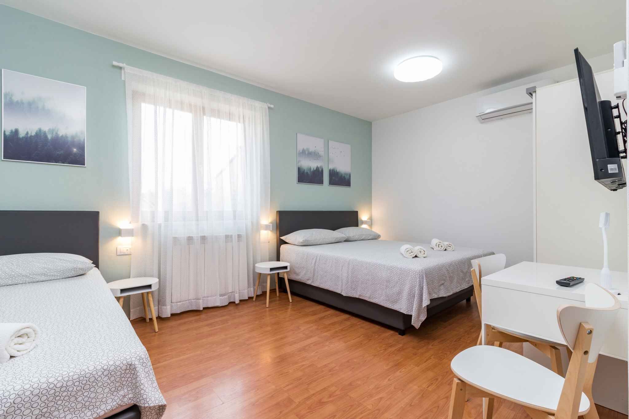 A hotel room with two beds, a desk, a chair, a TV, and a window with curtains.