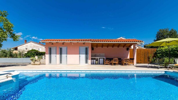 A poolside villa with a tiled pool, outdoor seating, and a wooden pergola. - Holiday apartment with swimming pool, playground and barbecue (Valbandon)