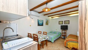 Uma cozinha compacta com pia e mesa de jantar, uma cama com cobertor colorido e uma televisão em um suporte.