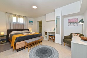 Ein modernes Schlafzimmer mit Bett, Nachttisch, Bank, Schreibtisch, Stuhl und Kunstwerk.