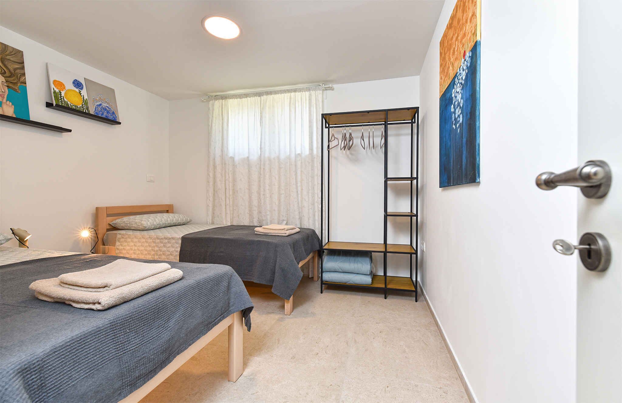 A room with two beds, a wardrobe, a painting, and a door with a handle.