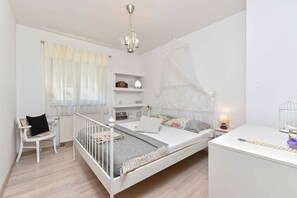 A white bedroom with a bed, a chair, a bedside table, a lamp, and a shelf with a clock. - Holiday apartment tastefully furnished with air conditioning (Pula)