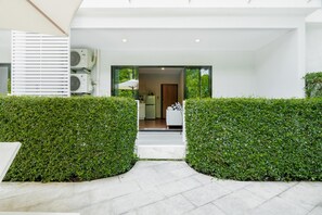 Entrada de un edificio moderno con un camino despejado, un interior blanco visible a través de la puerta y un espacio exterior blanco con una silla blanca.