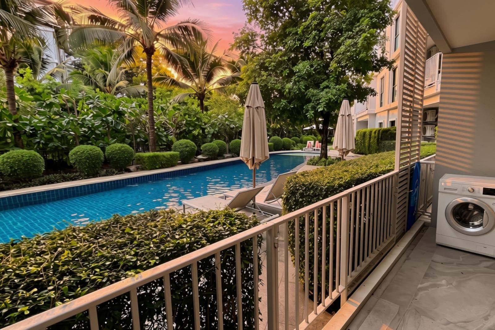 A poolside area with a view of a swimming pool, surrounded by lush greenery and palm trees.