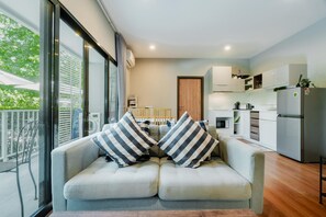 Una sala moderna con un sofá y una mesa de comedor, una cocina con armarios y electrodomésticos blancos, y un balcón con vistas a zonas verdes.