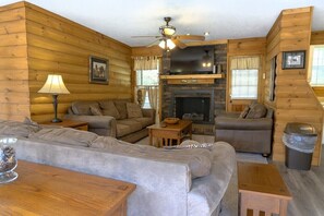 A log cabin interior with a fireplace, two sofas, a coffee table, and a ceiling fan. - Hoot N Holler:  5-Bedroom -Walk to downtown Pigeon Forge (Pigeon Forge)