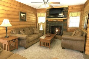 A log cabin interior with a fireplace, a television, and a ceiling fan. - Hoot N Holler:  5-Bedroom -Walk to downtown Pigeon Forge (Pigeon Forge)