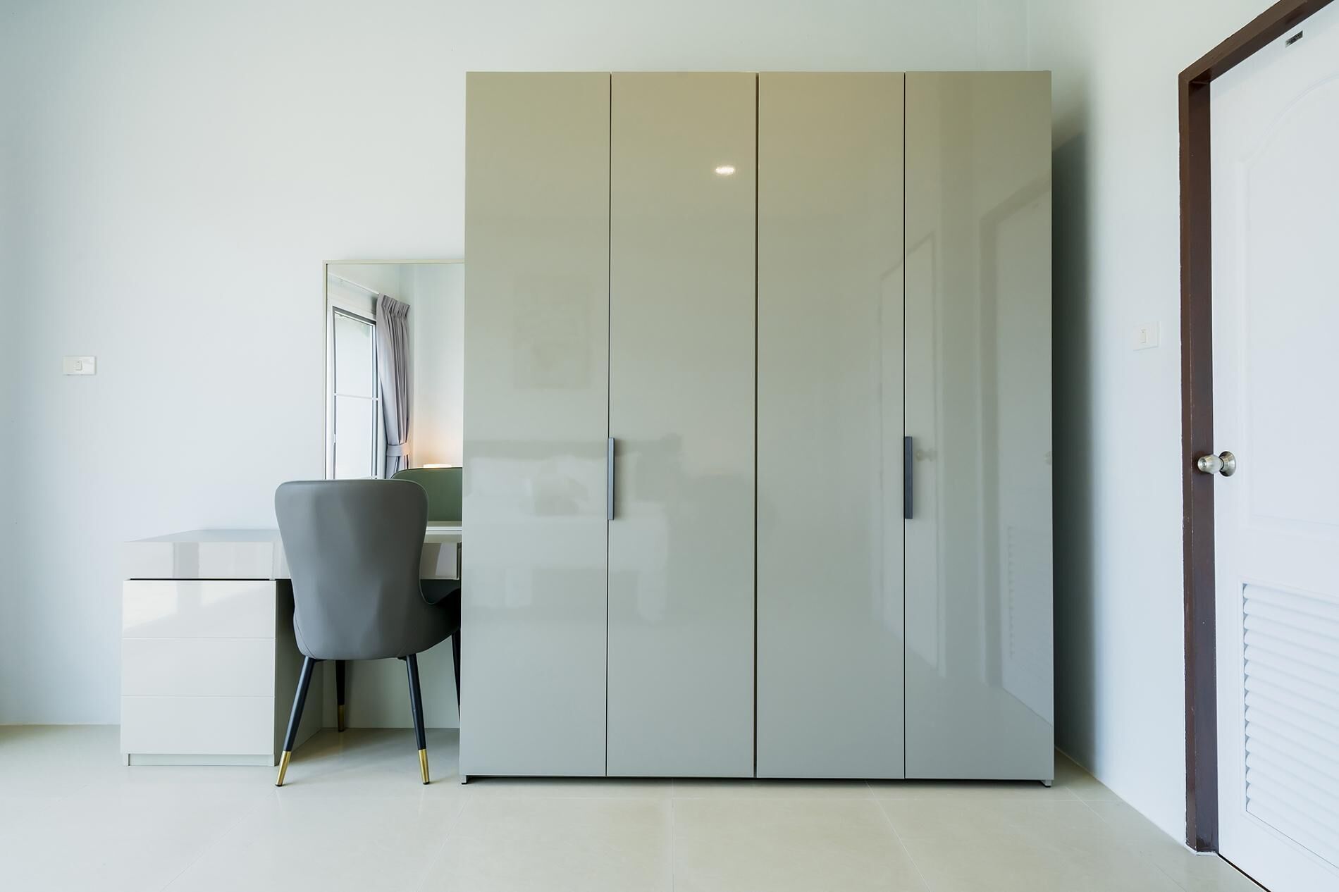 Ein Zimmer mit großem Kleiderschrank, Schreibtisch und Stuhl sowie einer Tür.