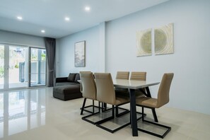 A modern dining area with a round table and six chairs, a sofa, and a large window with curtains. - Boathouse 4 Bed Townhouse Fully Renovated Rawai (Rawai)