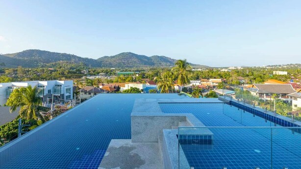 Piscina no terraço com painéis solares, rodeada por edifícios e palmeiras, com vista para colinas distantes.