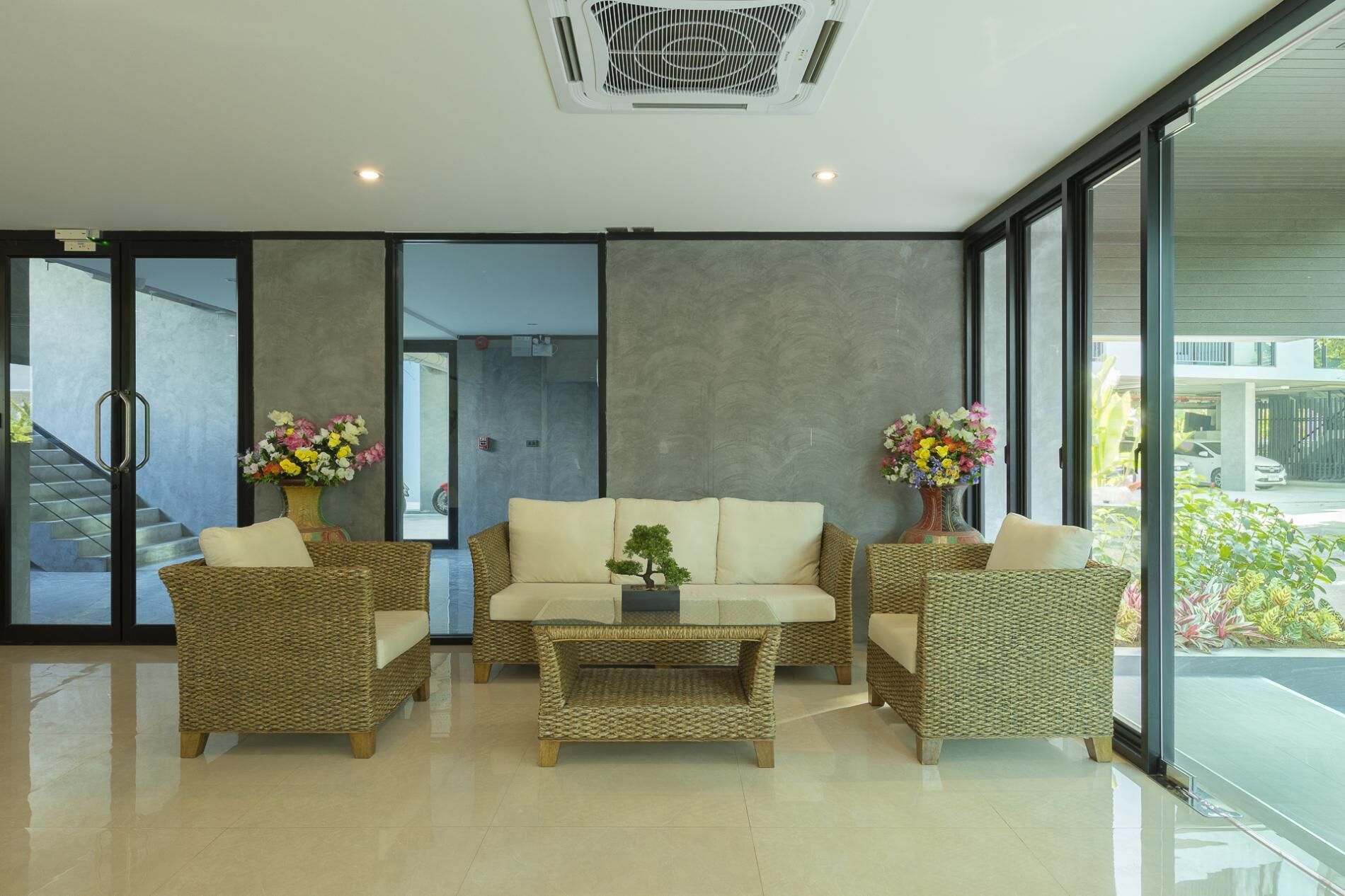 A modern interior with a sofa set, wicker chairs, a coffee table, and large windows offering a view.