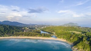 Paisagem costeira com praia, colinas arborizadas e uma cordilheira distante.