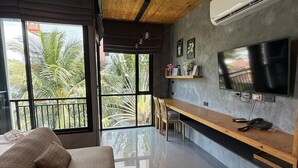 Sala de estar moderna com sofá, televisão, área de jantar e varanda com vista para palmeiras.