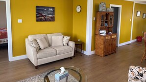 Un salon avec un canapé, une table basse en verre, un meuble en bois et un tableau accroché au mur.