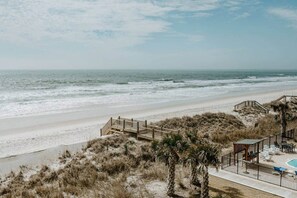 A beach view with a wooden walkway leading to a pool area with lounge chairs and umbrellas. - Dune Not Disturb | Luxury Getaway North Topsail (North Topsail Beach)