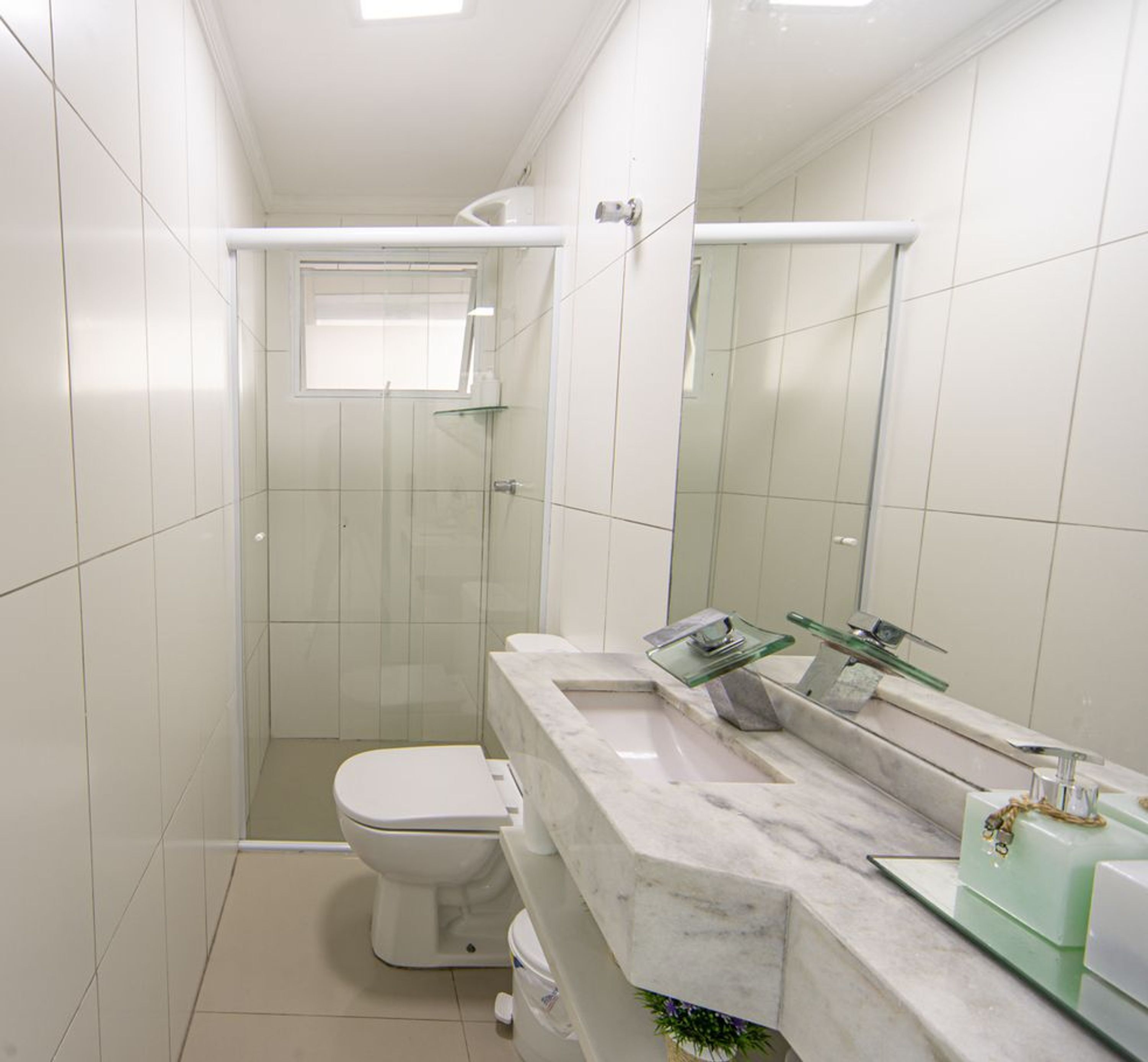 Une petite salle de bain comprenant des toilettes, une douche en verre et un lavabo en marbre avec un porte-savon en verre.