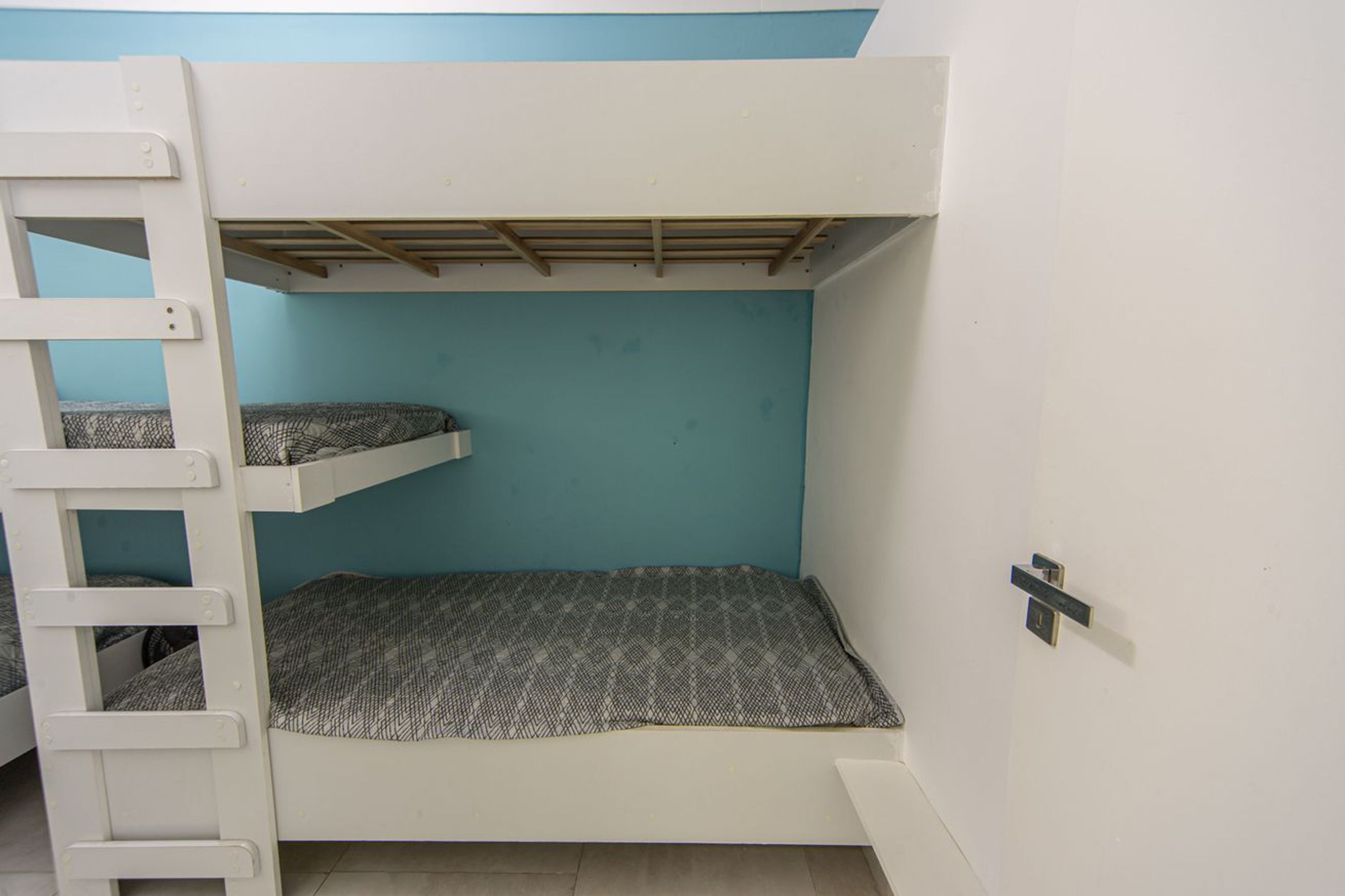 A bunk bed room with a ladder, a blue wall, and a white floor.