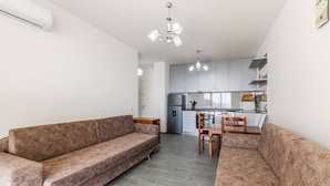 A modern living space with a sofa, dining table, chairs, kitchen area, and ceiling light fixture. - Beachfront Apartment With Pool Access (Shengjin)