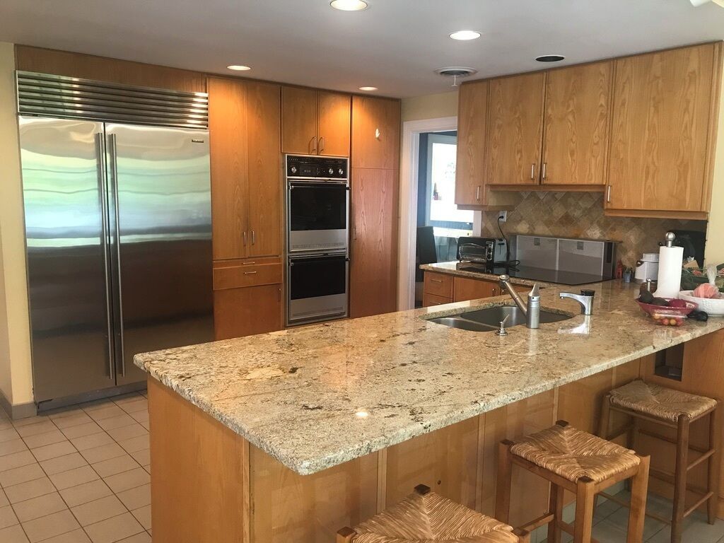A kitchen with a stainless steel refrigerator, double oven, granite countertop, wooden cabinets, and a built-in microwave.