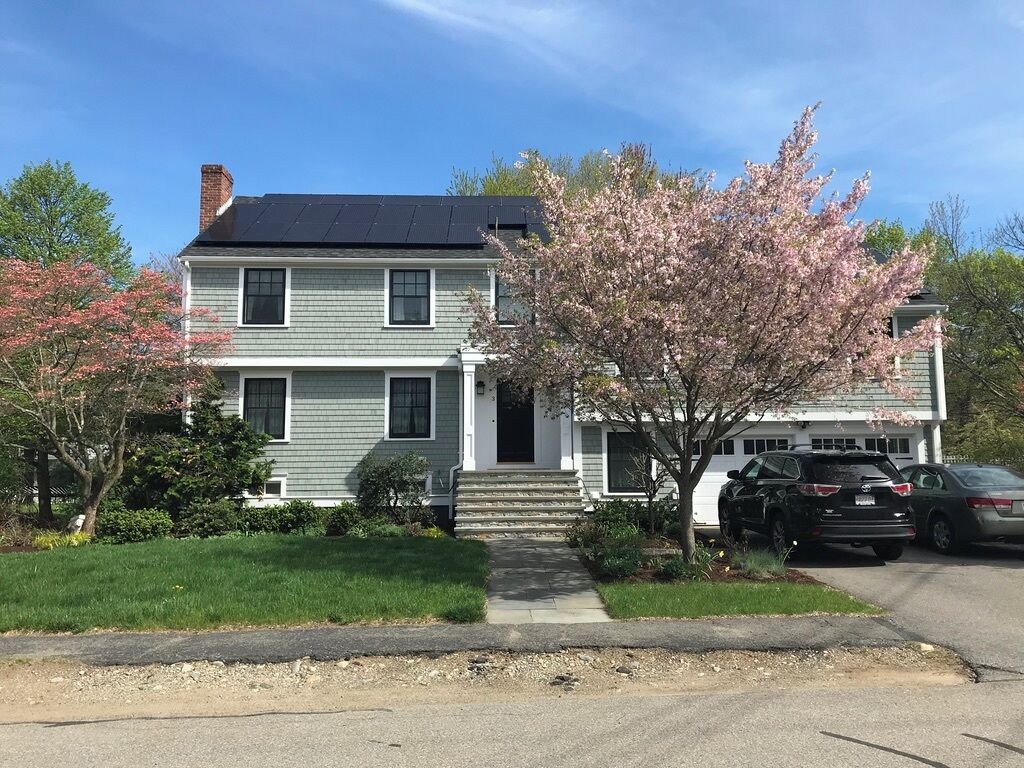 A two-story house with a front porch, a driveway, and parked cars.