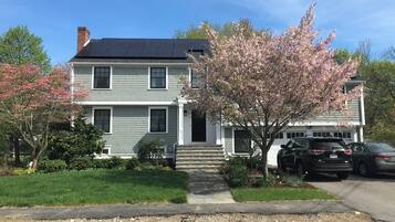 A two-story house with a front porch, a driveway, and parked cars.