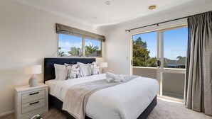 A modern bedroom with a large bed, a nightstand, a lamp, and a view of the outdoors through a sliding door.