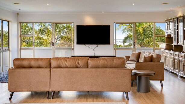 A modern living room with a large sofa, a smaller armchair, a TV mounted on the wall, and a cabinet with drawers.