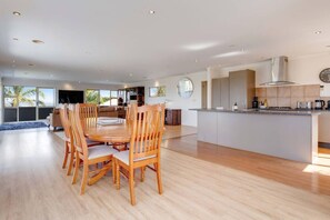 Una cocina moderna con una isla central, comedor con sillas de madera y vistas al exterior.