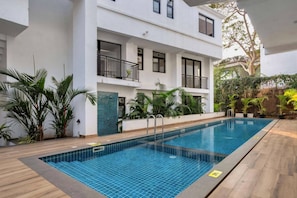 A swimming pool with tiled edges, surrounded by a wooden deck and potted plants. - Casa Solana 4bhk Villa w Private Pool nr Candolim (Candolim)