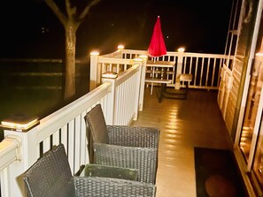 A deck with wicker chairs and a red umbrella, a white railing, and a table with chairs.