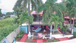 Un bâtiment à deux étages doté d’un balcon, de palmiers et d’un espace extérieur aménagé pour s’asseoir.