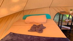 Una tenda amb un llit, una almoina, una manta i una taula petita amb una planta.