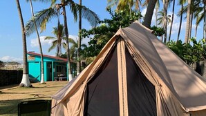 Una tenda muntada en una zona verda amb palmeres al fons.