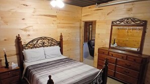 Un dormitorio con paneles de madera, con cama, cómoda y espejo.