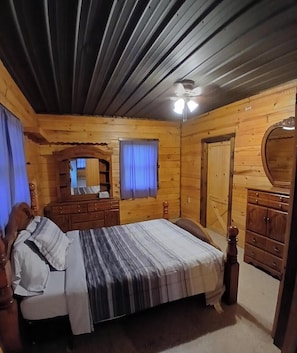 A wooden cabin bedroom with a bed, dresser, mirror, and ceiling fan. - Cozy 4-bedroom cabin close to Rathbun lake with AC comfort (Moravia)