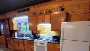 Una cocina con armarios de madera, estufa, pileta y refrigerador.