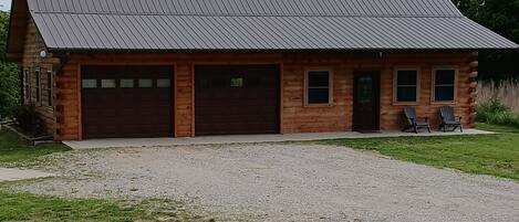 A log cabin with a metal roof, two garage doors, and a gravel driveway.