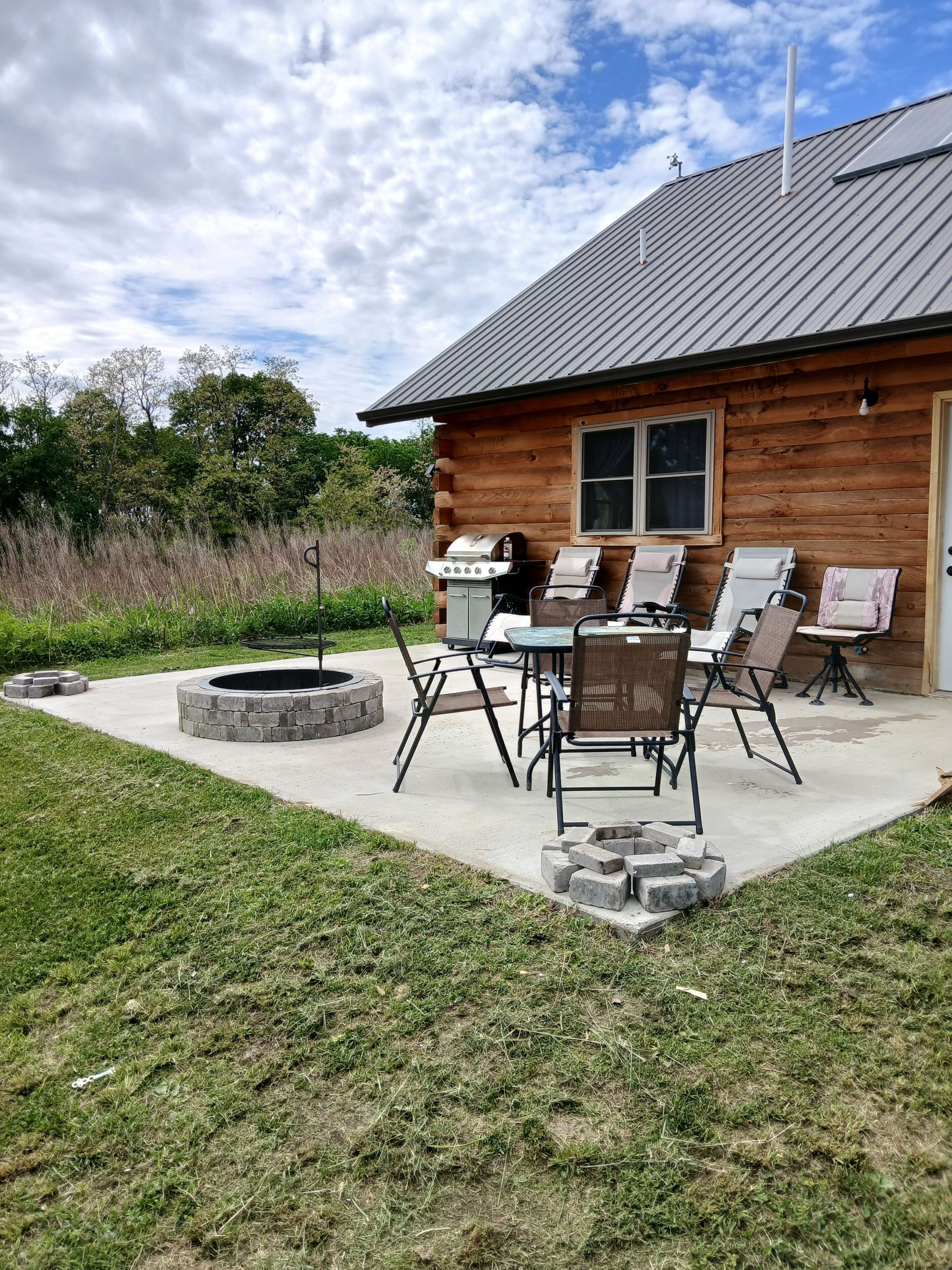 A wooden cabin with a patio, outdoor seating, a fire pit, and a grill.