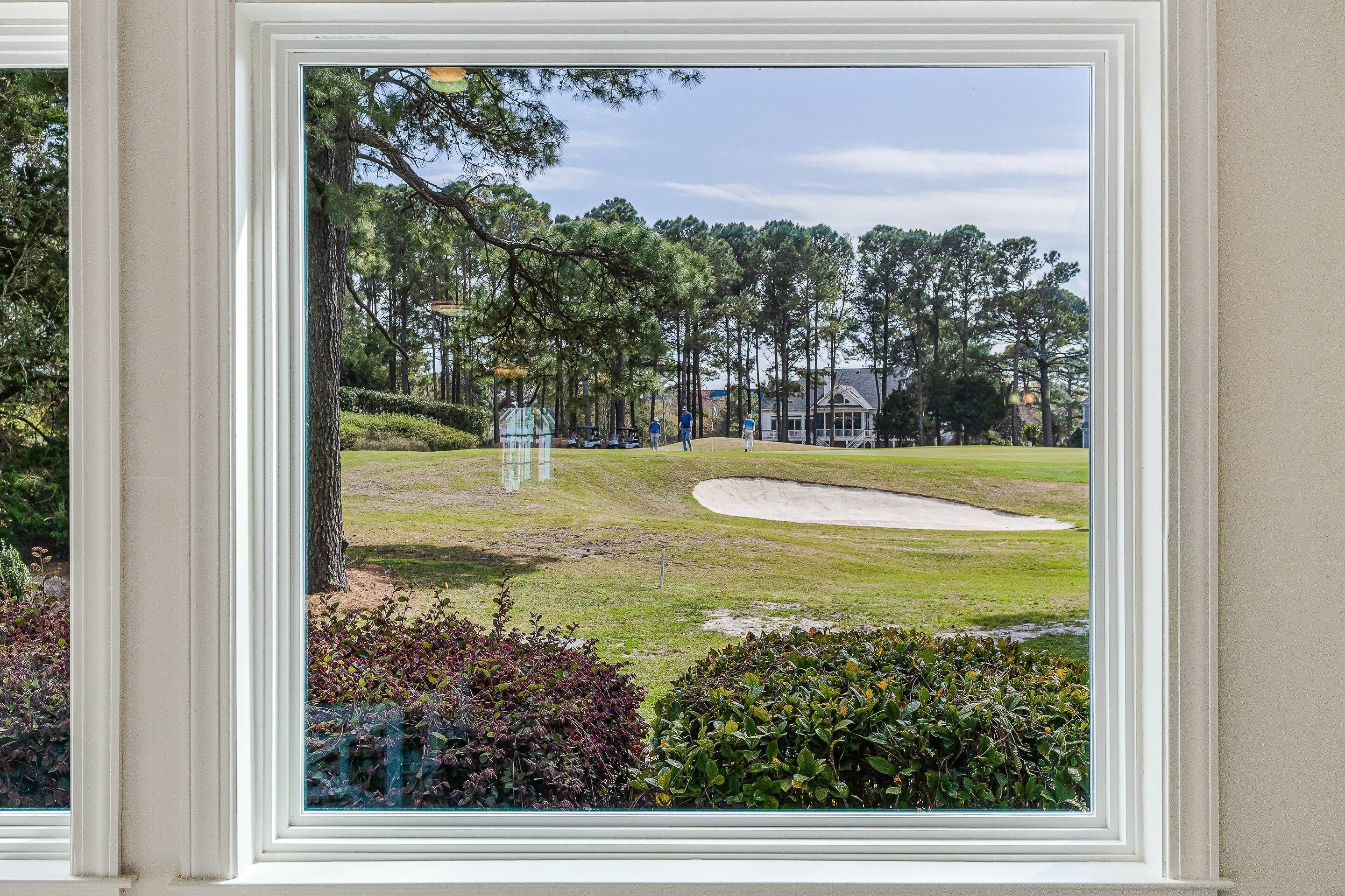A view through a window of a golf course with a sand bunker and trees.