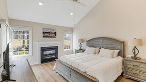 Une chambre à coucher avec un grand lit, une cheminée, un ventilateur de plafond et une vue sur l’extérieur.