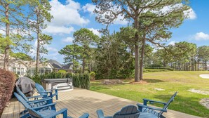 Une terrasse avec des fauteuils Adirondack et un barbecue, entourée d’arbres et d’une pelouse.