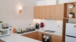 Eine moderne Küche mit Holzschränken, einer weißen Arbeitsplatte, einem eingebauten Backofen, einer Mikrowelle und einer Kaffeemaschine.
