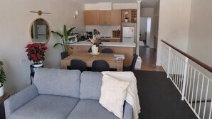 Ein modernes Wohnzimmer mit grauem Sofa, einem Esstisch und einer Küche im Hintergrund.