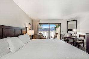 Une chambre d’hôtel avec un grand lit, un bureau, une chaise et un balcon offrant une vue sur les montagnes.