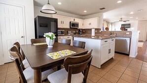 Una cocina moderna con armarios blancos, una isla central y un comedor con mesa y sillas.