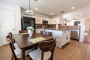 A modern kitchen with white cabinets, a central island, and a dining area with a table and chairs. - Charming 3-bedroom bungalow with AC in cozy Frisco (Frisco)