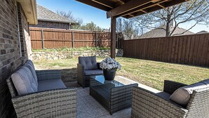 Un patio al aire libre con mobiliario de mimbre, un muro de piedra y una valla de madera al fondo.