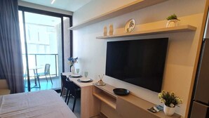Et moderne hotelværelse med en stor seng, et skrivebord med et fladskærms-tv, et lille tekøkken og en balkon med en stol.