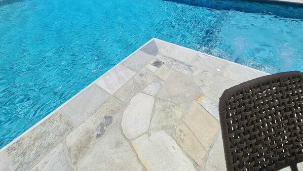 En swimmingpool med havudsigt, en overdækket terrasse og en fliseterrasse af sten.